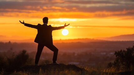 Silhouette of a man in a suit standing on a hilltop at sunset, arms outstretched in celebration