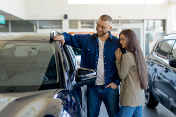 Young couple happily checking out vehicle in dealership showroom, millennial man inspecting car...