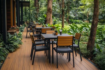 Empty outdoor cafe table and chairs on green grass in a tropical garden, with black steel-frame chairs and wood slat backrests.
