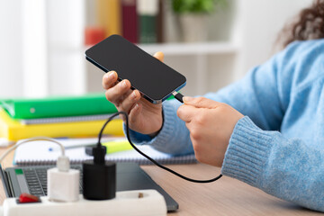 Close up of a business woman hand plugging charger cable to a smart phone at home