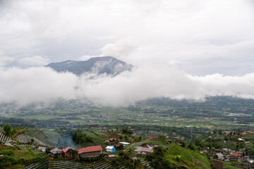 Scenic view of Mount Marapi with clouds hovering above lush green villages and terraced fields in West Sumatera, Indonesia. 