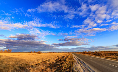 A road stretches across a dry, empty field with a clear blue sky above