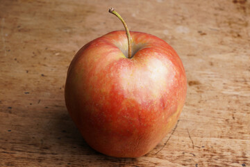 Fresh red apple resting on a wooden surface in daylight