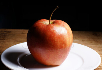 Red apple placed on a white plate with dark background