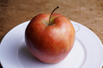 Freshly picked apple on a white plate against wooden background