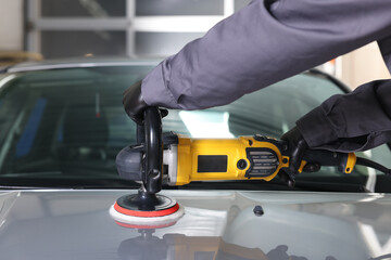 Man polishing car hood with orbital polisher indoors, closeup