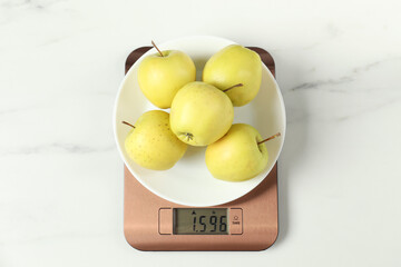 Modern electronic kitchen scale with apples on white marble table, top view