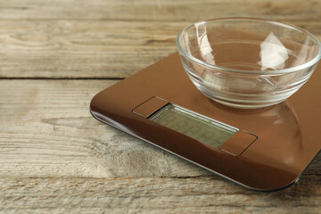 Electronic kitchen scale with empty bowl on wooden table, closeup. Space for text