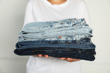 Woman with stack of different stylish jeans near light wall indoors, closeup