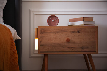 Glowing modern LED lamp on wooden bedside table indoors