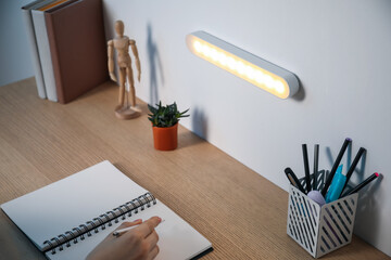 Woman working at desk with LED lamp on wall, closeup