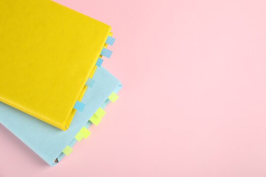 Books with colorful tabs on pink background, top view. Space for text