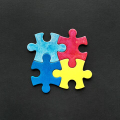 Obraz premium Four colorful puzzle pieces in red, blue, yellow, and light blue arranged together on a black background
