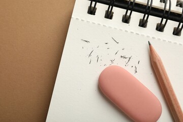 Eraser, pencil, scraps and notebook on brown background, top view