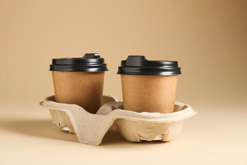Paper coffee cups in cardboard holder on beige background