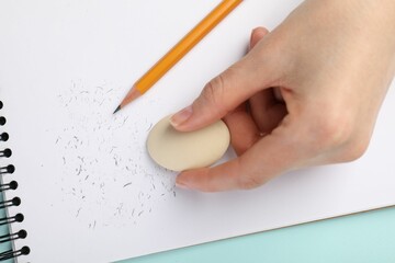 Woman rubbing eraser against paper at light blue table, closeup