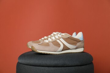Pair of stylish sneakers on pouf against red background. Space for text
