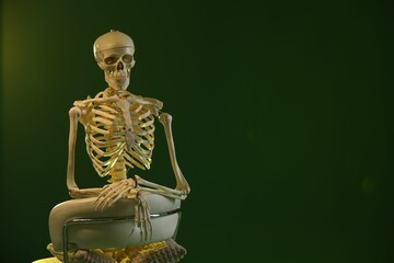 Artificial human skeleton model sitting and chair on green background, space for text