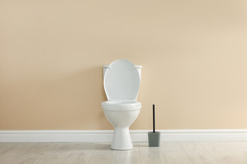 Toilet bowl and brush on floor near beige wall in restroom