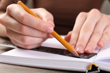 Woman drawing sketch with ruler and pencil on notebook at wooden table, closeup