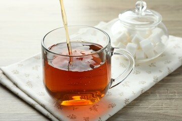 Pouring freshly brewed tea from teapot into cup at wooden table, closeup