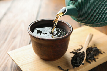 Pouring freshly brewed tea from teapot into cup at table, closeup