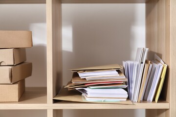 Different paper envelopes and parcels on wooden shelves in post office