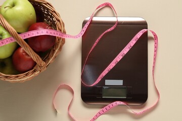 Electronic kitchen scale, measuring tape and basket of apples on beige table, flat lay. Diet