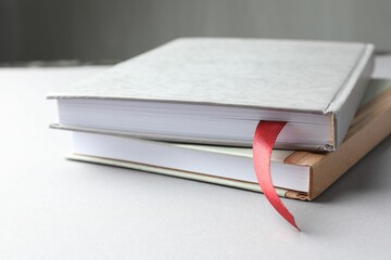 Book with red ribbon bookmark and colorful one on light table against grey background, closeup