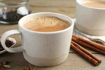 Aromatic Masala tea in cups and spices on wooden table, closeup