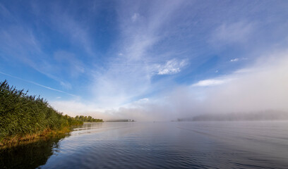 A foggy morning with a blue sky and a lake