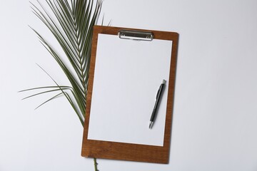 Clipboard with blank paper, pen and palm leaf on white background, flat lay