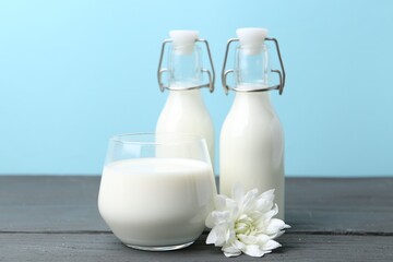 Fresh milk and flower on wooden table against light blue background