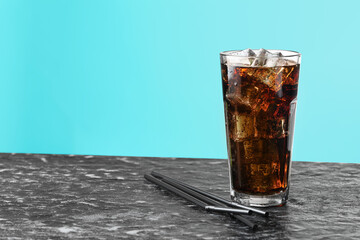 Refreshing cola with ice cubes in glass and straws on dark textured table against turquoise gradient background, closeup. Space for text