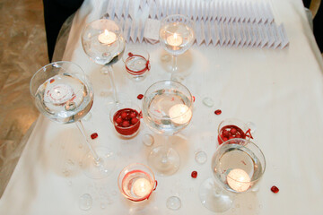 Table decoration with candles in glasses and red accents on white cloth