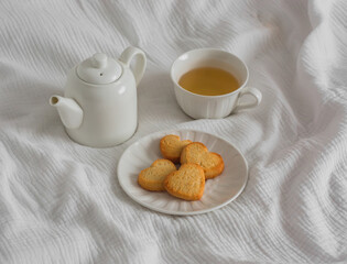A cup of green tea, shortbread cookies in the shape of a heart, a teapot on a light background