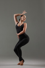 Stylish dancer posing in black bodysuit with expressive posture on gray background.