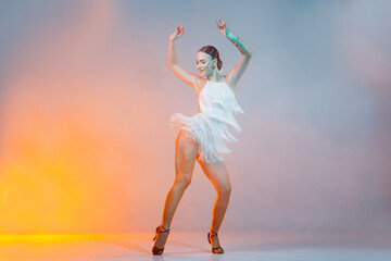 Smiling female dancer performing on stage in fringe dress with colorful studio lights and smoke.