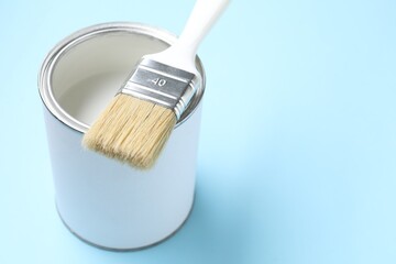 Can of white paint and brush on light blue background, closeup. Space for text