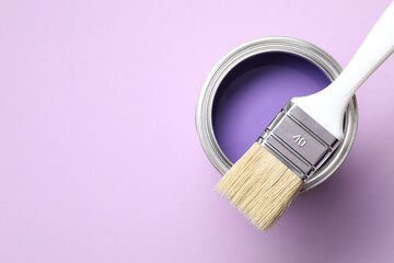 Can of bright paint and brush on violet background, top view. Space for text