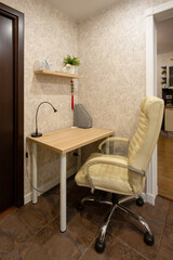 Apartment interior. Leather chair near a small desk. Desk lamp on the desk. Shelf on the wall. Compact work area in the hallway of a small apartment. Writing corner. Home mini-office.
