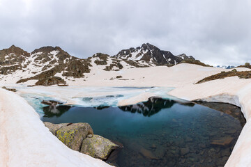 Melting snow reveals rugged peaks and frozen lakes in the Pyrenees of Lleida, Spain. A stunning contrast between winter and spring, capturing untouched nature and alpine beauty along the GR11 trail.