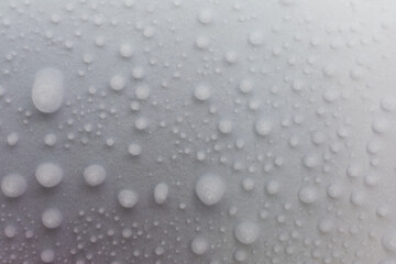 Close-up of a white surface covered with many small frozen water droplets. The droplets are scattered across the surface, creating a frosty texture.