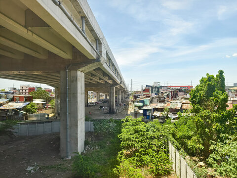 Paranaque, Metro Manila - April 12, 2025: A concrete flyover from the CAVITEX&ndash;C-5 Link slices through a dense informal settlement, highlighting stark urban inequality.