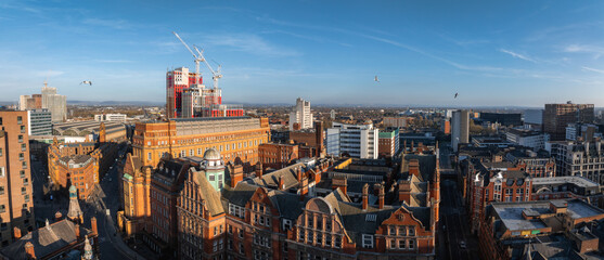 Aerial view of Manchester, UK, on a sunny day showing red brick buildings, cranes, a skyscraper...