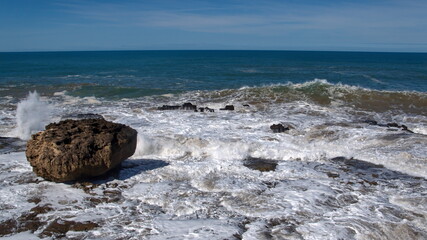 Waves breaking around a large boulder on the rocky coastline just below the old city walls of the medina in Essaouira, Morocco
