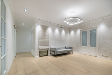 Spacious living room with light walls and laminate flooring. White doors with glass windows. Modern sofa with pillows.