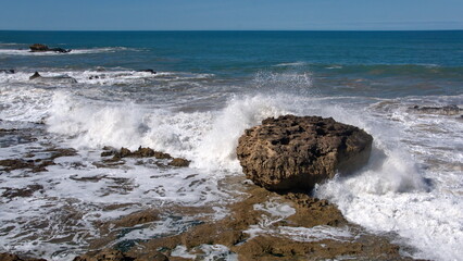 Waves breaking around a large boulder on the rocky coastline just below the old city walls of the medina in Essaouira, Morocco