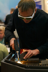 male welder at the workplace welds parts, sparks from welding, welder's protective helmet