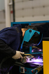 male welder at the workplace welds parts, sparks from welding, welder's protective helmet